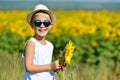 Adorable laughing blond boy in sun glasses and hat with sunflower on field outdoors Royalty Free Stock Photo