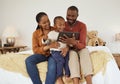 Adorable little african american boy using digital tablet while sitting on a bed with his parents. Young mother and Royalty Free Stock Photo