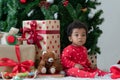 Adorable little African kid boy in red clothes sitting with gift boxes, toys, bear doll, Santa hat and Christmas tree