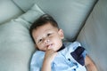 Adorable little Asian baby boy sucking finger in mouth lying on gray sofa Royalty Free Stock Photo