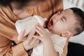 Adorable little Asian baby uncomfortable crying during drinking from baby bottle. Mother holding adorable her son with milk Royalty Free Stock Photo