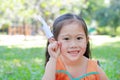 Adorable little Asian child girl fold a piece of white paper to rocket and showing on her forefinger in the green garden outdoor