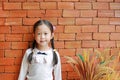 Adorable little Asian child girl lean against the red brick wall with decorative grass flower