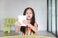 Adorable little Asian child girl is playing with educational colors flashcards while sitting at table in children room