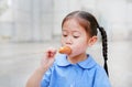 Adorable little Asian child girl in school uniform enjoy eating sausage
