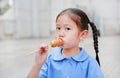 Adorable little Asian child girl in school uniform enjoy eating sausage