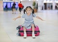Adorable little asian girl at airport sitting on suitcase with open arm