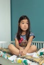 Adorable little asian girl child with stuffed animal toy sits in lotus position in nursery at home