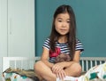 Adorable little asian girl child with stuffed animal toy sits in lotus position in nursery at home