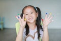 Adorable little Asian girl with colorful fingers painted in the children room