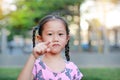 Adorable little Asian girl in garden with pointing at camera. Portrait smiling kid in park. Focus at child face