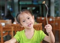 Adorable little Asian girl holding knife and fork sitting on wood chair at restaurant having breakfast Royalty Free Stock Photo