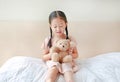 Adorable little Asian girl playing teddy bear while sitting on the bed at home