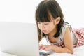 Adorable Little Asian girl playing or watching videos on laptop computer while lying on the bed in a relaxed atmosphere at home. Royalty Free Stock Photo