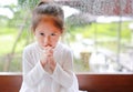 Adorable little Asian girl praying at glass windows on the raining day. Spirituality and religion Royalty Free Stock Photo