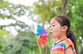 Adorable little Asian kid girl blowing wind turbine in the summer garden Royalty Free Stock Photo