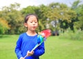 Adorable little Asian kid girl blowing wind turbine in the summer garden Royalty Free Stock Photo