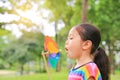 Adorable little Asian kid girl blowing wind turbine in the summer garden Royalty Free Stock Photo