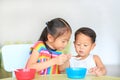 Adorable little Asian sister and her little brother eating cereal with cornflakes and milk together and friendly on the table.