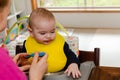 Adorable little baby boy in feeding chair being spoon fed by his mother Royalty Free Stock Photo