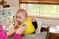 Adorable little baby boy in feeding chair being spoon fed by his mother Royalty Free Stock Photo