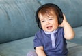 Adorable little baby boy listening to music in headphones on his head sitting on blue sofa at home Royalty Free Stock Photo