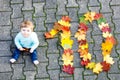 Adorable little baby girl in autumn park on sunny warm october day with oak and maple leaf Royalty Free Stock Photo