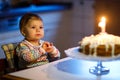 Adorable little baby girl celebrating first birthday. Child blowing one candle on homemade baked cake, indoor. Royalty Free Stock Photo