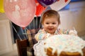 Adorable little baby girl celebrating first birthday. Baby eating marshmellows decoration on homemade cake, indoor. Royalty Free Stock Photo