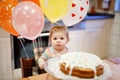 Adorable little baby girl celebrating first birthday. Baby eating marshmellows decoration on homemade cake, indoor Royalty Free Stock Photo