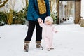 Adorable little baby girl making first steps outdoors in winter through snow. Cute toddler learning walking. Mother Royalty Free Stock Photo