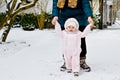 Adorable little baby girl making first steps outdoors in winter through snow. Cute toddler learning walking. Mother Royalty Free Stock Photo