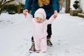 Adorable little baby girl making first steps outdoors in winter through snow. Cute toddler learning walking. Mother Royalty Free Stock Photo