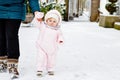 Adorable little baby girl making first steps outdoors in winter through snow. Cute toddler learning walking. Mother Royalty Free Stock Photo