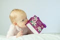 Adorable little baby lying on the white blanket and holding purple gift bag in his hands. Horisontal studio shot. Happy Royalty Free Stock Photo