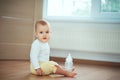 Adorable little baby sitting in bedroom on the floor with bottle with milk or water and laughing. Infant Childhood Kids People Royalty Free Stock Photo