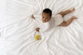 Adorable Little Black Baby Boy Lying On Bed Next To Rattle Toy Royalty Free Stock Photo