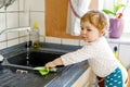 Adorable little blond baby girl washing dishes in domestic kitchen. Royalty Free Stock Photo