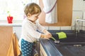 Adorable little blond baby girl washing dishes in domestic kitchen. Royalty Free Stock Photo