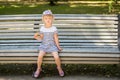 Adorable little blond girl sitting on a bench in a city park and eating cone ice-cream Royalty Free Stock Photo