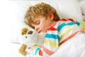 Adorable little blond kid boy in colorful nightwear clothes sleeping and dreaming in his white bed with toy. healthy Royalty Free Stock Photo