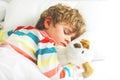 Adorable little blond kid boy in colorful nightwear clothes sleeping and dreaming in his white bed with toy. healthy Royalty Free Stock Photo