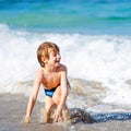 Adorable little blond kid boy having fun on ocean beach. Excited child playing with waves, swimming, splashing and happy Royalty Free Stock Photo