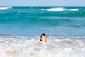 Adorable little blond kid boy having fun on ocean beach. Excited child playing with waves, swimming, splashing and happy Royalty Free Stock Photo