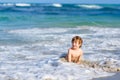 Adorable little blond kid boy having fun on ocean beach. Excited child playing with waves, swimming, splashing and happy Royalty Free Stock Photo