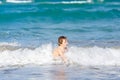 Adorable little blond kid boy having fun on ocean beach. Excited child playing with waves, swimming, splashing and happy Royalty Free Stock Photo