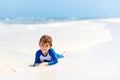 Adorable little blond kid boy having fun on tropical beach of carribean island. Excited child playing and surfing in sun