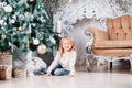 Adorable little blonde girl in a blue jeans sitting on a floor near christmas tree and looking on toy. Royalty Free Stock Photo