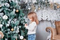 Adorable little blonde girl in a blue jeans sitting on a floor near christmas tree and looking on toy. Royalty Free Stock Photo