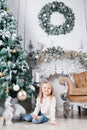 Adorable little blonde girl in a blue jeans sitting on a floor near christmas tree and looking on toy. Royalty Free Stock Photo